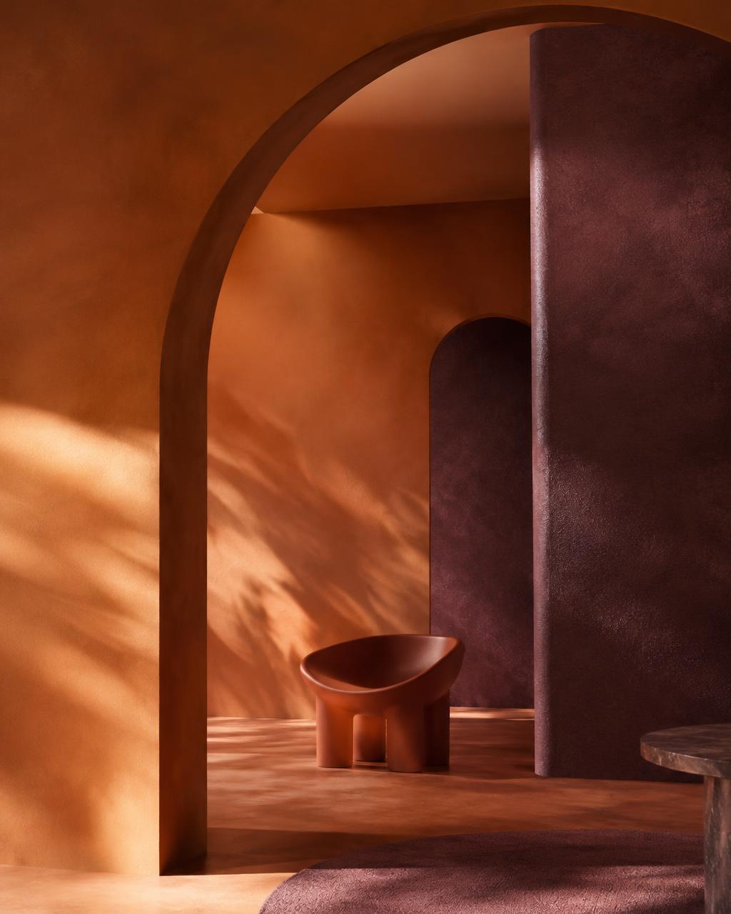 Sunlit terracotta arches and a sculptural chair in a plum-toned interior